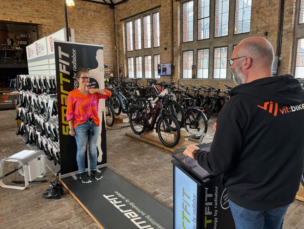 Ein Mann und eine Frau nutzen fröhlich einen Vermessungscomputer in einem Fahrradgeschäft, um sich besser für ein neues Fahrrad entscheiden zu können