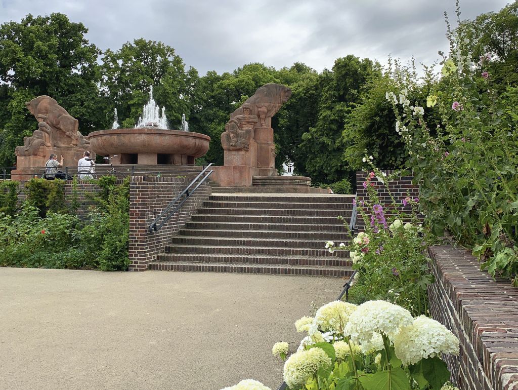 parkanlage mit mauern aus backstein, großer brunnen aus rotem stein