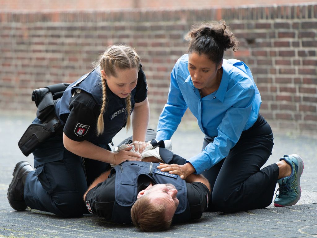 zwei Polizistinnen knien über einem angeschossenen polizisten