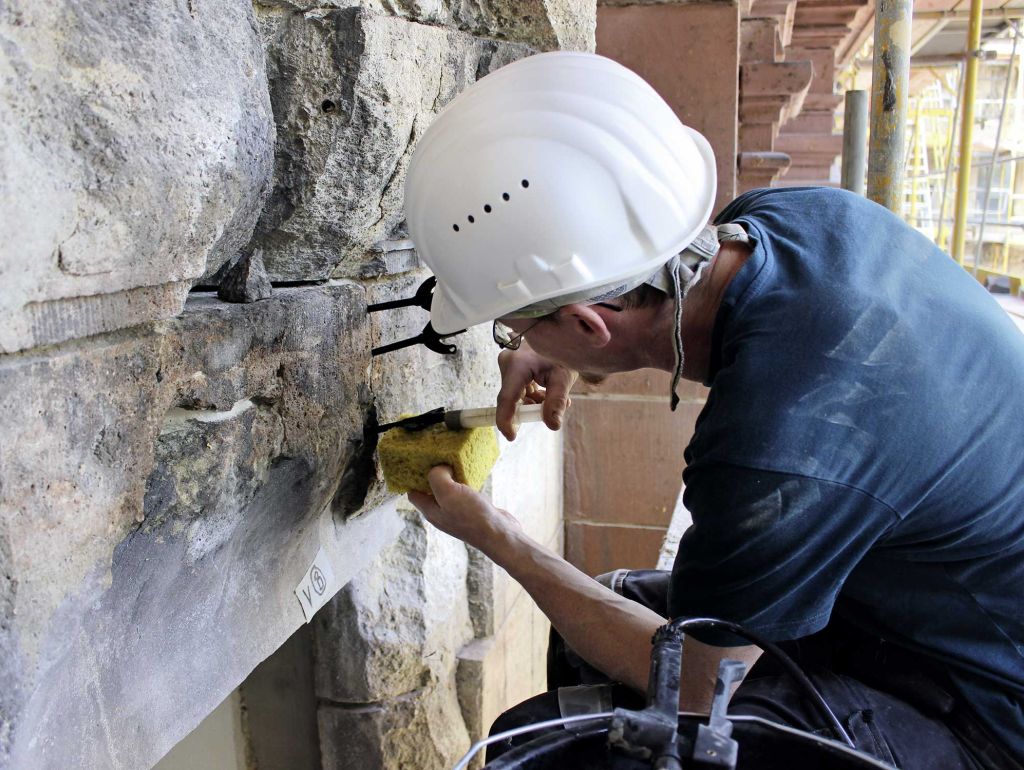 Bauarbeiter mit Helm spritzt etwas in die Fassade 