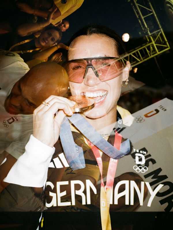 Frau mit Fußball-Medaille. Auf ihrem Pulli steht Germany. Sie lächelt. 