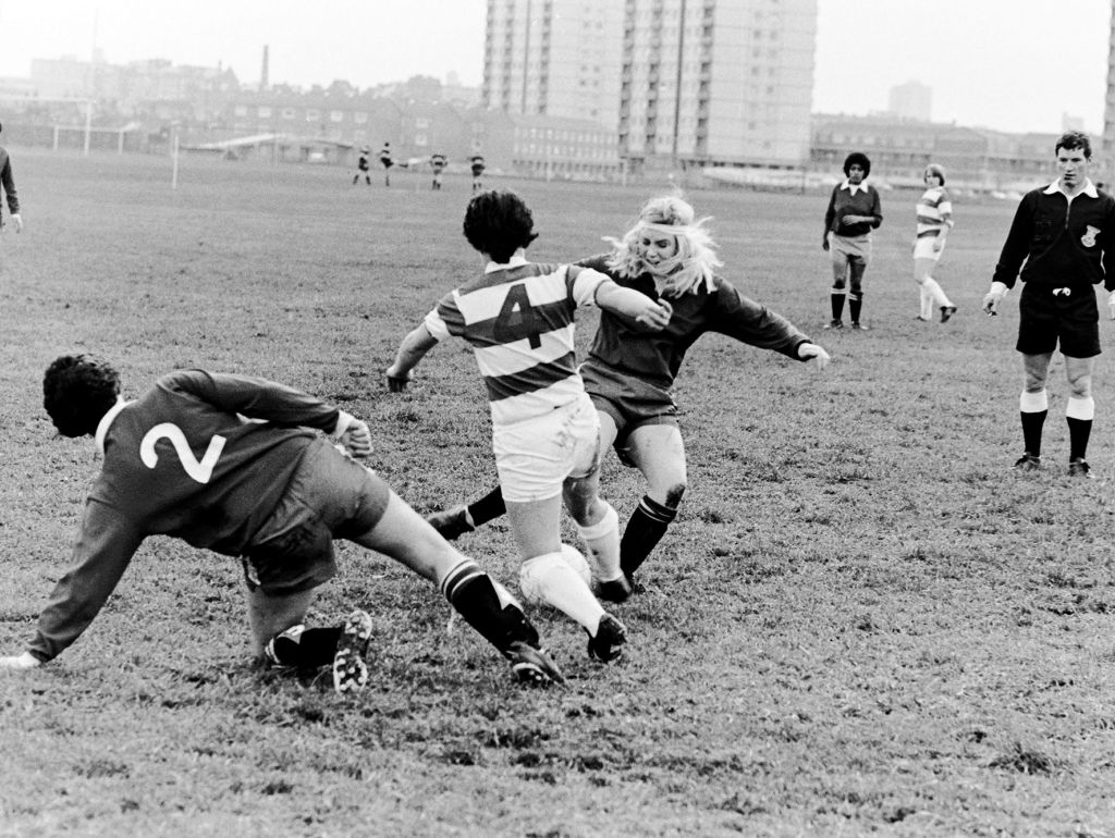 Schwarzweißfoto von Frauen die Fußball spielen in einer urbanen Umgebung.