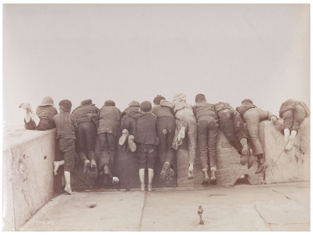 Schwarz-weiss Foto von einer Gruppe von jungen menschen die sich über eine Mauer lehnen.