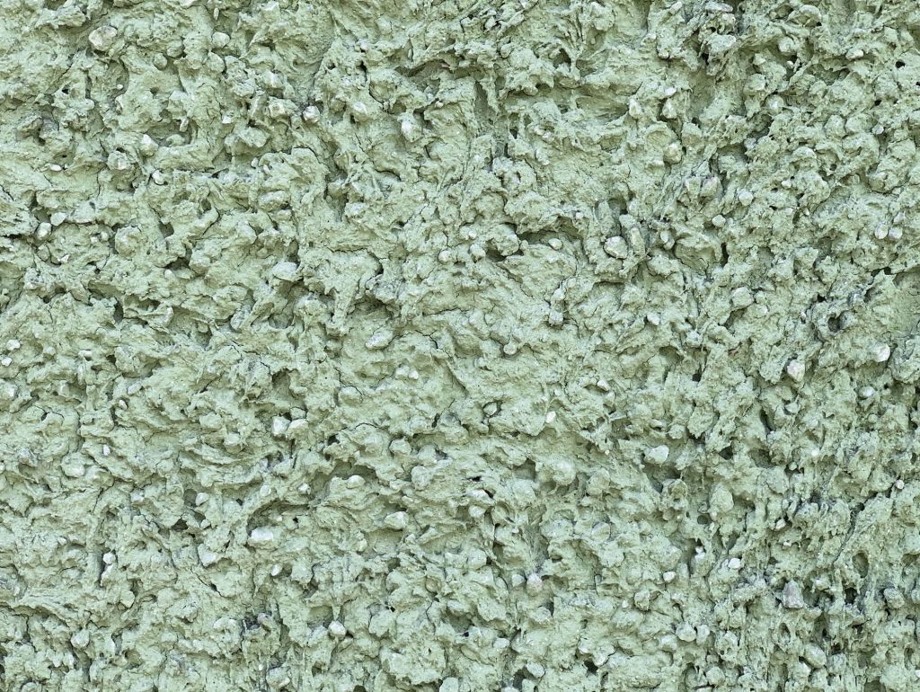 Nahaufnahme einer rauen, hellgrün gestrichenen Wand mit unregelmäßiger, körniger Oberfläche.