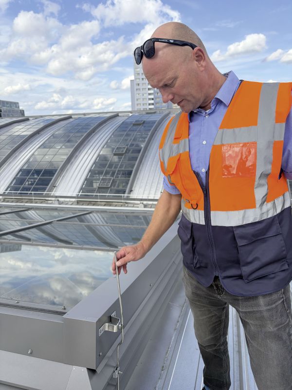 Ein Mitarbeiter in Warnweste überprüft mit einem Werkzeug die Dachkonstruktion des Berliner Ostbahnhofs. Im Hintergrund sind die großen Glasflächen und geschwungenen Dachfenster zu sehen.