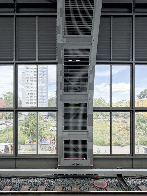 Blick durch die großen Fenster eines Bahnhofs auf umliegende Gebäude, Bäume und Straßen. Im Vordergrund sind Gleise und eine massive Stahlkonstruktion zu sehen. Es ist Taubenschutzgitter aus pulverbeschichtem Aluminium statt wie früher Stahlnetze 