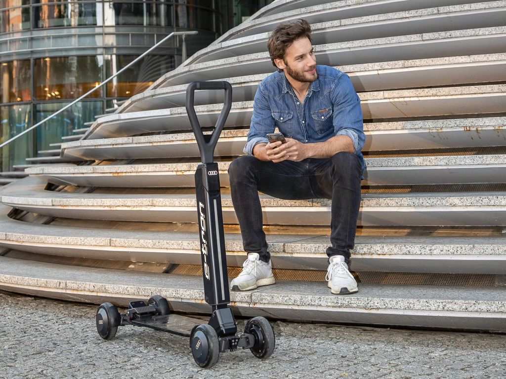 Mann sitzt auf einer Treppe vor ihm ein E-Scooter, Skateboard Hybrid