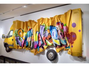 ein halbes Postauto an der wand, zusammengeknautscht und besprüht mit einem Graffitto