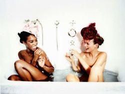 Naomi Campbell und Kate Moss sitzen in einer mit Wasser gefüllten Badewanne. Sie lächeln und scheinen sich zu amüsieren.